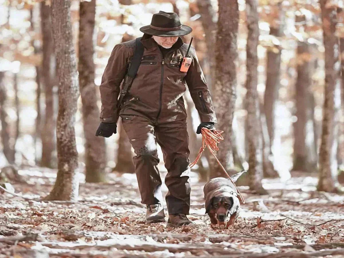 Jäger mit Hund im Wald in brauner Hillman 6OL Jagdjacke und passender 6OL Jagdhose bei der Outdoor-Jagd.