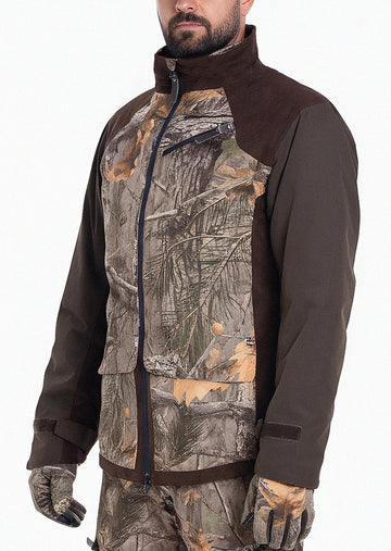 Eine Person, die die Hillman Tarnjacke Jagd | Jagdjacke Camouflage - Fusion 3DX mit Tarnmuster und einfarbig braunen Ärmeln trägt, steht vor einem unifarbenen Hintergrund. Nur die untere Hälfte des Gesichts ist sichtbar, was diese elegante Jagdjacke hervorhebt.