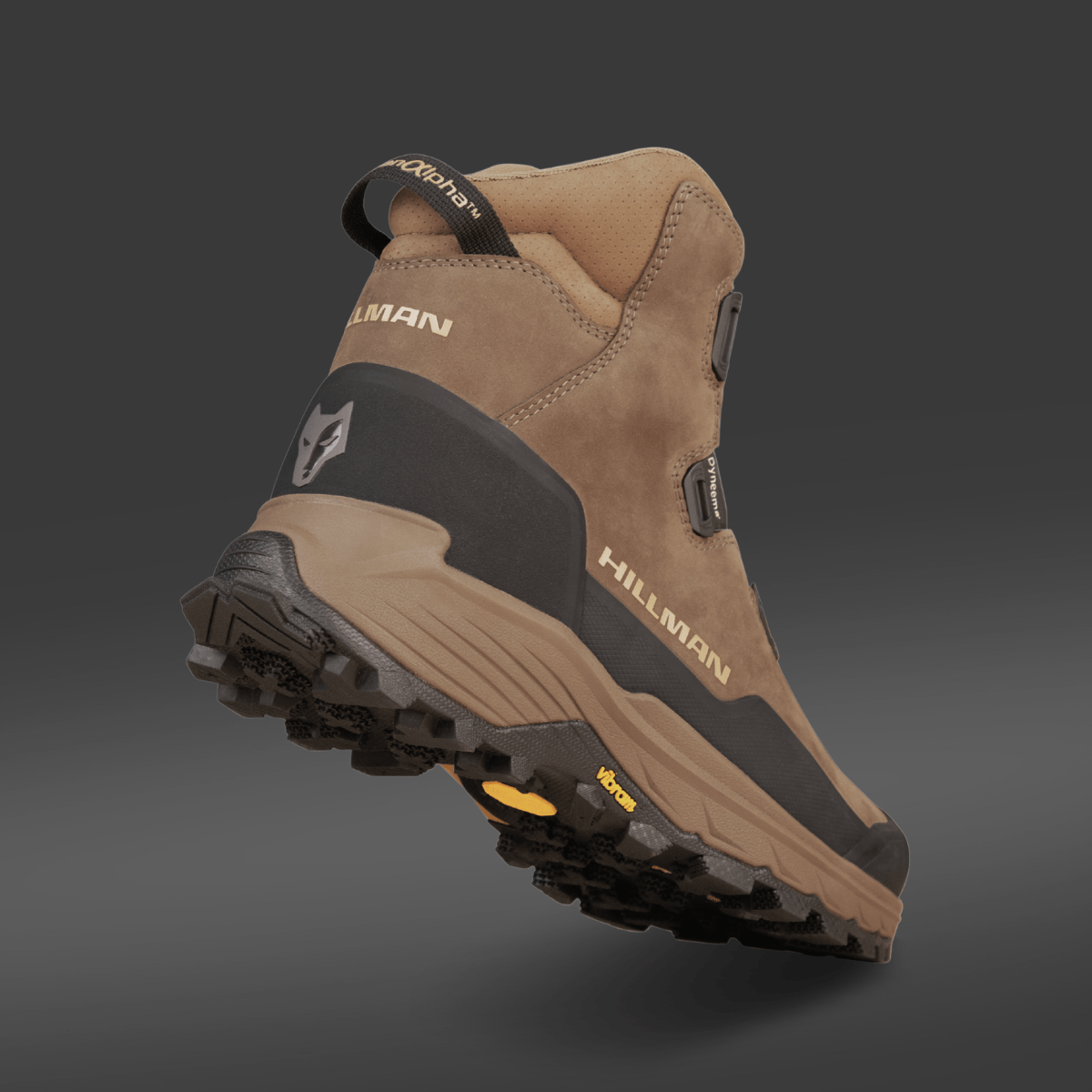 Ein brauner und schwarzer Jagdstiefel Wasserdicht - Herren Jagdschuhe | Alpha DryHunt™ Wanderstiefel von Hillman wird aus einem niedrigen Winkel von hinten auf einem grauen Hintergrund gezeigt, mit einer robusten Sohle und einem Wolfslogo an der Ferse.