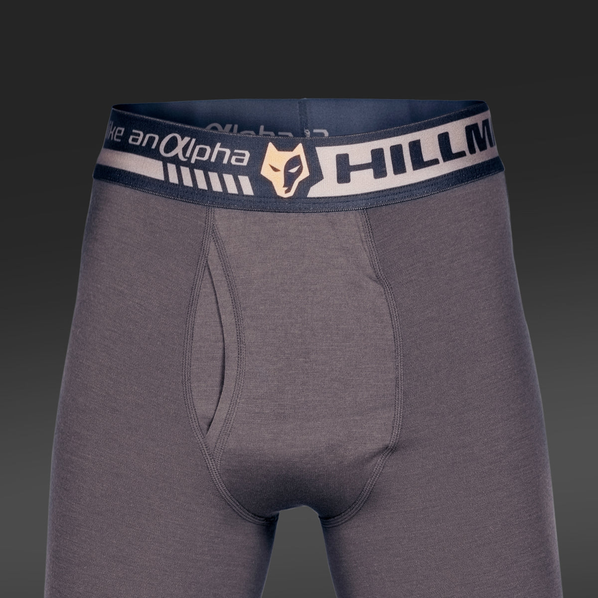 Graue Herren-Boxershorts mit dunklem Bund, der „Hillman“ und ein stilisiertes Fuchs-Logo zeigt. Sie bestehen aus Bambusfaser, bieten ein geschmeidiges, körperbetontes Tragegefühl und verfügen über einen Hosenschlitz. Der Hintergrund ist in einem dunkelgrauen Farbverlauf gehalten.