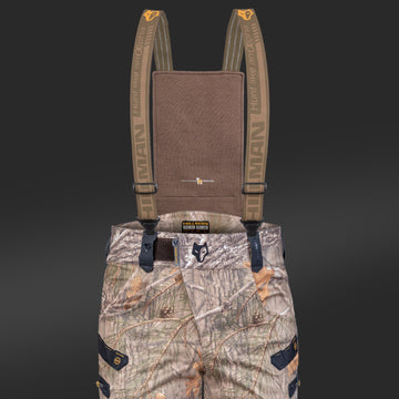 Die Hillman "6OL Winter Jagdhose Camouflage" ist eine wasserdichte Jagdhose mit Hosenträgern im Waldmuster. Die Tarnhose verfügt über mehrere Taschen und eine robuste Textur, ideal für Outdoor-Aktivitäten. Der Hintergrund ist dunkelgrau.