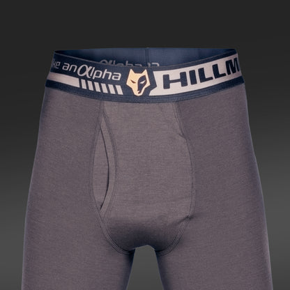 Graue Herren-Boxershorts mit dunklem Bund, der „Hillman“ und ein stilisiertes Fuchs-Logo zeigt. Sie bestehen aus Bambusfaser, bieten ein geschmeidiges, körperbetontes Tragegefühl und verfügen über einen Hosenschlitz. Der Hintergrund ist in einem dunkelgrauen Farbverlauf gehalten.