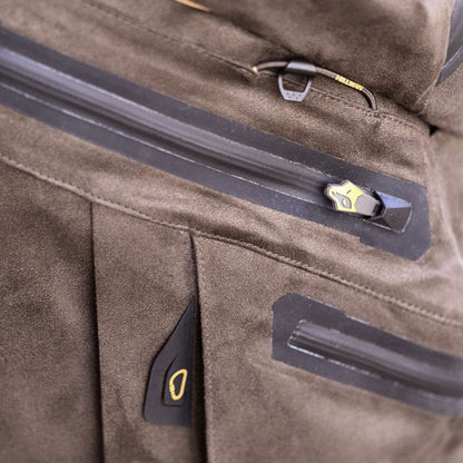 Nahaufnahme einer braunen Wildlederjacke mit sichtbaren eckigen Nähten und einem eleganten schwarz-goldenen Reißverschluss, der an Hillmans 6OL Winter Jagdhose Camouflage – Tarnhose erinnert. Der weich strukturierte Stoff verfügt über einen kleinen, funktionalen Haken über dem Reißverschluss.