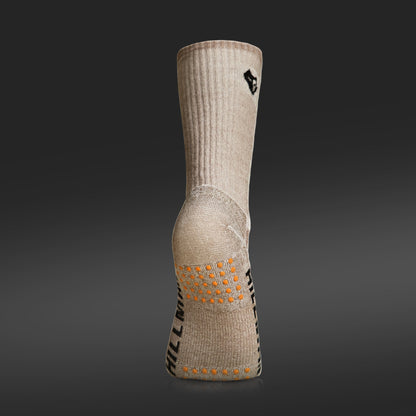Eine einzelne JAGDSOCKEN MERINOWOLLE ULTRAWARME [HC] von Hillman®GWR aus isolierender Naturfaser, beige mit gerippter Struktur und orangefarbenen Grip-Pads an der Sohle. Sie hat eine Fersennaht und schwarzen Text an der Seite auf dunklem Hintergrund mit Farbverlauf.